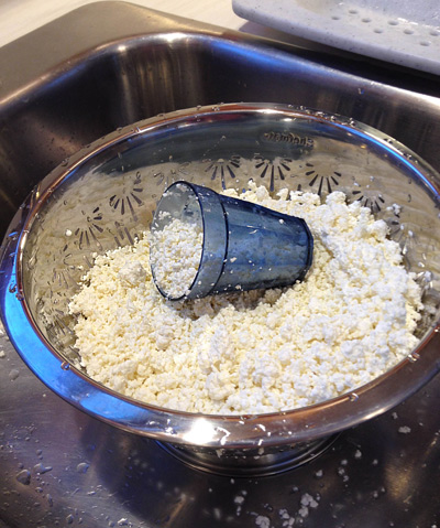 I moved the salted curds back to the colander in case they have any more draining to do while I scoop them into the press. The little blue juice glass is just the right size to transfer curds to the press, a little at a time.